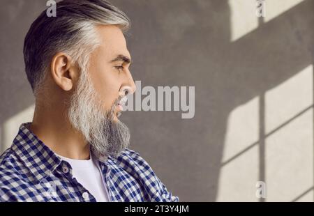 Ritratto ravvicinato in profilo di un uomo maturo barbuto sicuro su sfondo grigio Foto Stock
