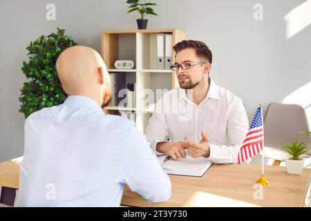 Console seduto alla scrivania con un giovane e parlando con lui del visto e dell'immigrazione negli Stati Uniti Foto Stock