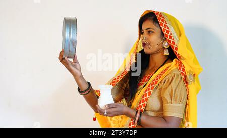 Donna indiana che tiene il filtro Karwa Chauth e il karwa o il karva di zucchero per la celebrazione Karwa Chauth isolato su sfondo bianco Foto Stock