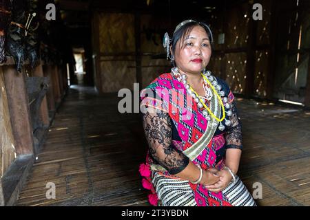 Donna della tribù Adi in abiti tradizionali seduta di fronte al muro decorata con guanto di toro in una tradizionale casa di legno ad Assam, nel nord-est dell'India Foto Stock