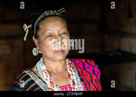 Ritratto di una donna della tribù Adi in abiti tradizionali, tipici orecchini in argento e copricapo in una tradizionale casa di legno ad Assam, nel nord-est dell'India Foto Stock