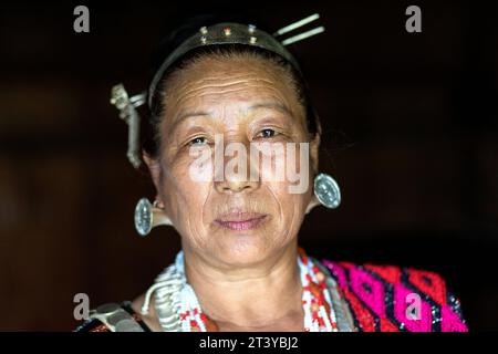 Ritratto di una donna della tribù Adi in abiti tradizionali, tipici orecchini in argento e copricapo in una tradizionale casa di legno ad Assam, nel nord-est dell'India Foto Stock