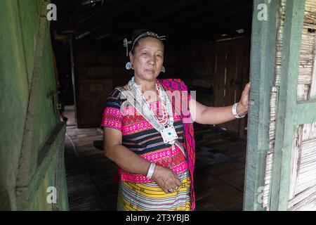 Ritratto di una donna della tribù Adi in abiti tradizionali, tipici orecchini in argento e copricapo in una tradizionale casa di legno ad Assam, nel nord-est dell'India Foto Stock