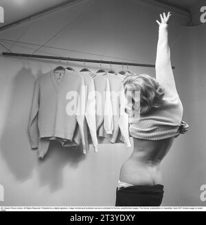 Negli anni '1950 Una giovane donna vista da dietro indossa un maglione a maniche lunghe. Di fronte a lei appendere capi di abbigliamento simili. Svezia 1955. Kristoffersson rif. BY91-1 Foto Stock