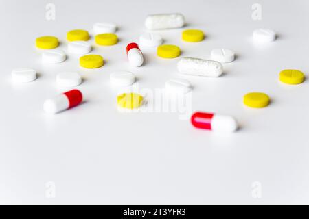 Compresse e pillole multicolore sparse su un tavolo bianco. Spazio di copia isolato per farmaco farmaceutico sfondo minimalista Foto Stock