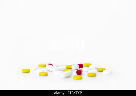 Pillole di medicinali multicolore sparse su un tavolo bianco. Capsule bianche, gialle e rosse. Spazio di copia isolato per farmaco farmaceutico sfondo minimalista Foto Stock