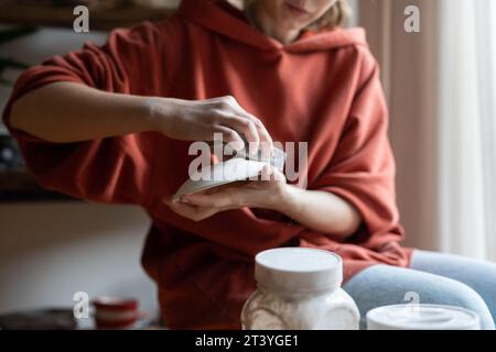 Primo piano mani ceramista donna con piattino e spugna dura per la lucidatura piatti dopo forno di ceramica Foto Stock