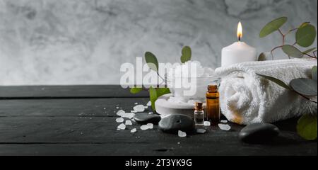 trattamento benessere e spa. articoli per la cura della pelle su un tavolo in legno nero con sfondo in marmo. oli essenziali, asciugamano, cristalli da bagno e candela Foto Stock