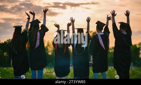 Sagome di laureati in abiti al tramonto che salutano il sole. Foto Stock