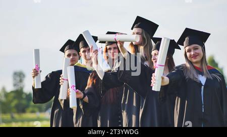 Allegri laureati che salutano i loro diplomi in una giornata di sole. Foto Stock