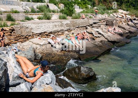 I turisti e la gente del posto si godono il sole estivo sulla spiaggia rocciosa vicino all'area turistica di Sovignion a Odessa, Ucraina. Il territorio è conosciuto come Miguel Beach. Foto Stock