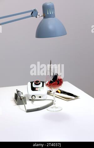 Concetto di San Valentino per manicure, pedicure, salone spa. Bicchiere di vino pieno di cuori rossi, smalto per unghie, olio, macchina per manicure professionale Foto Stock