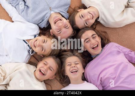 Un gruppo di sei ragazze felici sdraiate sulle spalle, che ridono e si divertono. Felice infanzia. Amici per sempre. Foto scattata dall'alto Foto Stock