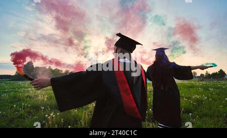 Gli studenti si laureano con fumo colorato che cammina attraverso il prato la sera. Foto Stock