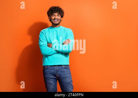 Foto di un arabo con capelli ricci che indossa un pullover color acquamarina con le mani incrociate sullo spazio di copia del cartellone, isolato su sfondo di colore arancione Foto Stock