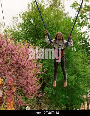 Rivne, Ucraina, 14 maggio 2022: Bambina gioiosa che salta su un banjo trampolino in un parco divertimenti Foto Stock