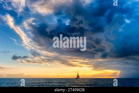 Una barca a vela si sta avvicinando A Una tempesta oceanica che si sta avvicinando con raggi solari che sfondano Foto Stock