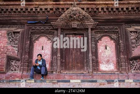 Kathmandu, Nepal, - 5 ottobre 2017: Uomo seduto vicino al muro del tradizionale tempio nepalese nel centro di Kathmandu Foto Stock