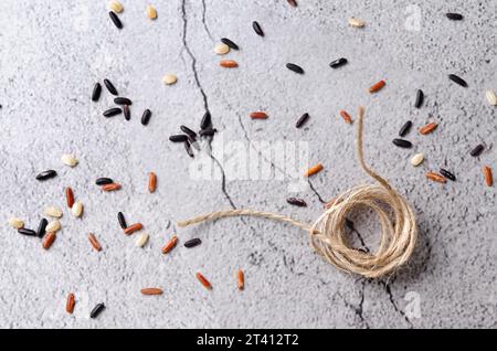 Un pezzo di filo rustico e chicchi di riso rosso, nero e bianco crudo su sfondo grigio-sassoso. Foto Stock