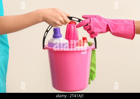 Mani femminili che tengono il secchio con prodotti per la pulizia su sfondo beige Foto Stock