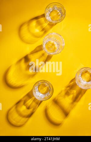 Composizione in bicchiere di whisky su sfondo giallo. I vetri vuoti sono sparsi sulla superficie del tavolo. Base piatta, vista dall'alto Foto Stock