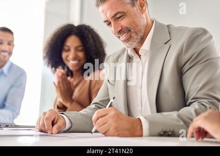 Buon vecchio uomo d'affari che firma un documento d'affari legale alla riunione del Consiglio. Foto Stock