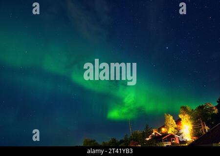 Una maestosa aurora boreale illumina il cielo sopra una rustica cabina di legno, emettendo un bellissimo bagliore verde e giallo Foto Stock