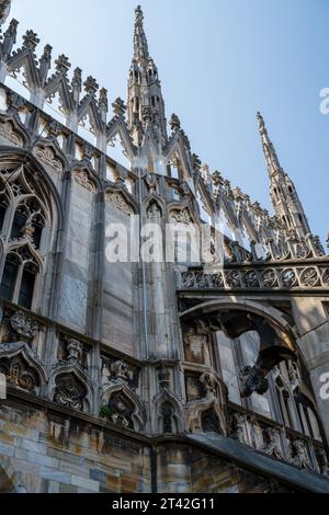 Vista laterale del Duomo di Milano dal passaggio pedonale sul tetto delle colonne, delle sculture e delle opere d'arte con sfondo blu del cielo. Foto Stock