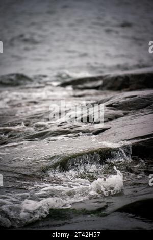 Un'immagine in bianco e nero ad alto contrasto di potenti onde che si infrangono su una spiaggia rocciosa Foto Stock