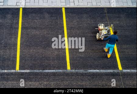 Un uomo maturo che porta generi alimentari in un carrello della spesa sta camminando verso la telecamera in una strada periferica Foto Stock