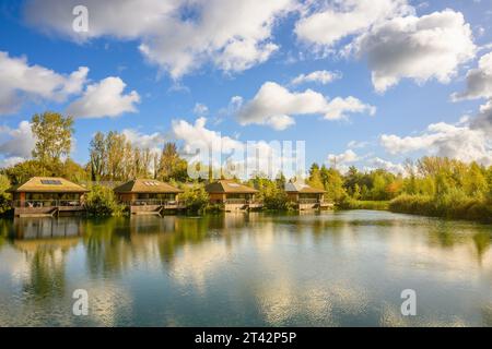 Un ambiente tranquillo caratterizzato da un gruppo di case in legno situate su di un lago idilliaco circondato da lussureggianti alberi verdi Foto Stock