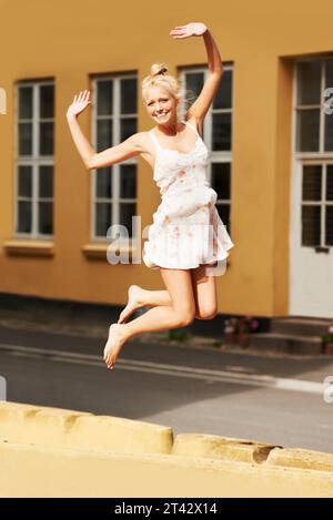 Ritratti, sorridi e salta con una donna durante l'estate nel suo quartiere per la libertà o l'energia per la vita. Moda, eccitata e giovane felice Foto Stock