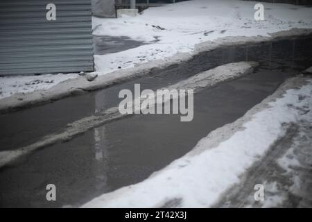 Neve fusa sulla strada. Grande pozzanghera in primavera. Molta acqua sull'asfalto. Scioglimento della neve in città. Foto Stock