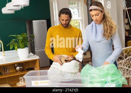 Coppia caucasica concentrata che smistano i rifiuti per riciclarli insieme in cucina, spazio per la copia Foto Stock