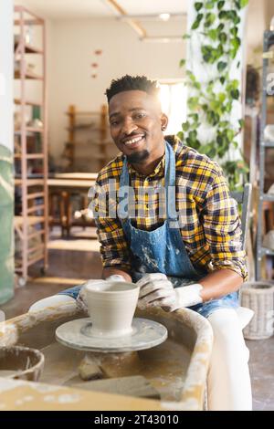 Felice ceramista afro-americano che lavora su un vaso di argilla usando la ruota di potter nello studio di ceramica Foto Stock