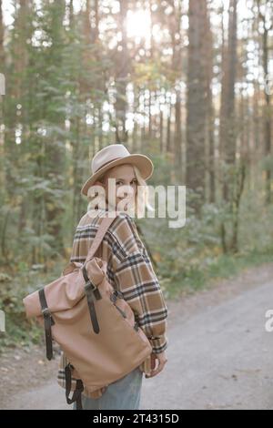 Donna elegante e sorridente in piedi nella foresta con uno zaino Foto Stock