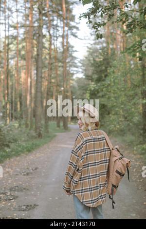 Donna elegante con una giacca a quadri in piedi in una foresta con uno zaino, Bielorussia Foto Stock