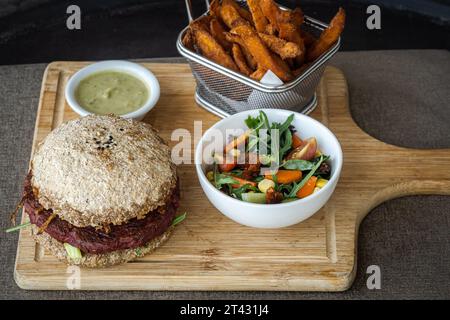 Primo piano di un hamburger di barbabietola e fagioli con patatine fritte dolci, insalata e salsa Foto Stock