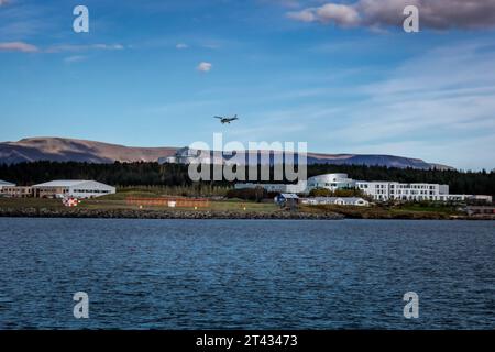 Reykjavik, Islanda - 25 settembre 2023: Paesaggio con aeroporto nazionale di Reykjavik e edificio Perlan. Un piccolo aereo in aria, una baia d'acqua di fronte. Foto Stock