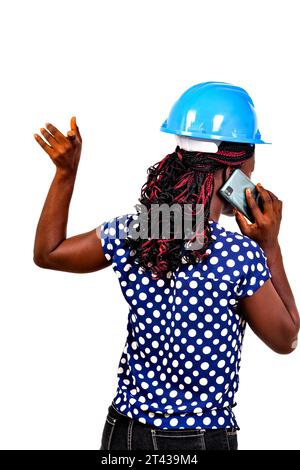 una bellissima ingegnere donna con casco di sicurezza in piedi su sfondo bianco che parla al telefono cellulare con la schiena alla fotocamera. Foto Stock