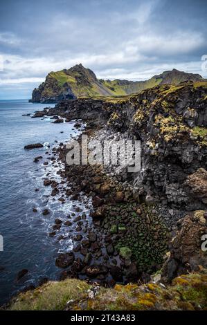 Scogliere rocciose sul lato ovest dell'isola islandese Heimaey in una giornata nuvolosa Foto Stock