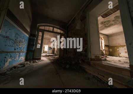 Dall'alto di un edificio abbandonato, dimora residenziale con pareti sporche e trasandate, camere spaziose, illuminate da finestre e pavimenti in macerie, con porta in vetro decorata ad arco Foto Stock
