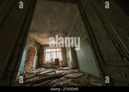 L'ingresso della hall dalla porta sporca, un mucchio di macerie con mobili rotti, sbucciati dalla vernice scavata nei muri di mattoni e finestre di vetro con recinzione alla luce del giorno, sotto il soffitto intemprato Foto Stock