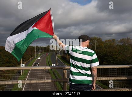 Leicester, Leicestershire, Regno Unito. 28 ottobre 2023. Un manifestante che indossa una camicia del Celtic Football Club sventola una bandiera durante una manifestazione pro-palestinese e lo striscione cade vicino alla base dei sistemi tattici UAV. UAV Tactical Systems è una società israeliana-francese che produce droni venduti all'esercito britannico, a Israele e ai mercati internazionali delle armi. Credit Darren Staples/Alamy Live News. Foto Stock