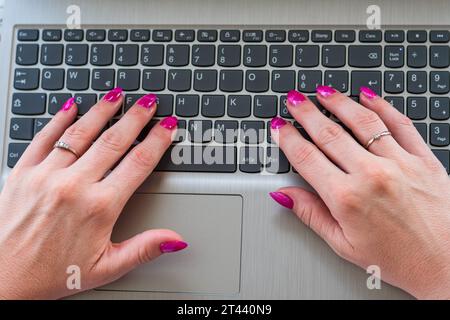 Donna che usa un notebook. Mani ravvicinate di una ragazza con smalto viola poggiato sulla tastiera di un notebook. Preso dall'alto. Foto Stock