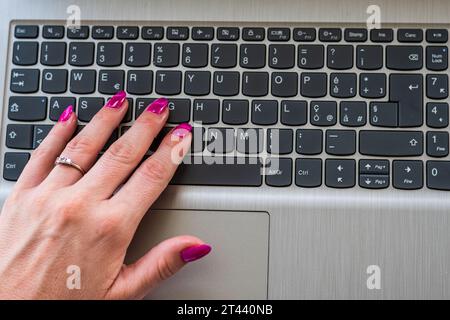 Donna che usa un notebook. Mano ravvicinata di una ragazza con smalto viola poggiato sulla tastiera di un notebook. Preso dall'alto. Foto Stock
