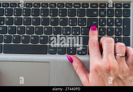 Donna che usa un notebook. Primo piano di una ragazza con smalto viola mentre si preme Invio sulla tastiera di un notebook. Preso dall'alto. Foto Stock
