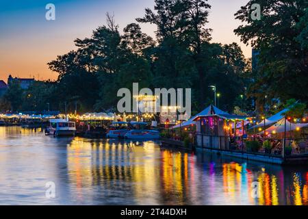 Wroclaw, Polonia - giugno 25 2023: Facciate di bar e ristoranti moderni sull'acqua vicino all'isola e piene di piccole luci accese intorno Foto Stock