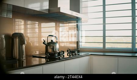 Cucina accogliente e contemporanea: Arredi interni luminosi e minimalisti, vista finestra, fiasca e bollitore in acciaio per cucinare a casa Foto Stock