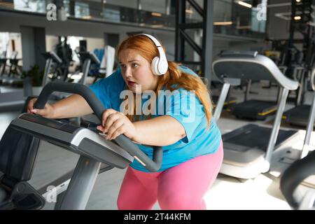 Una donna in sovrappeso, pazza e motivata, cavalca velocemente sulla cyclette Foto Stock